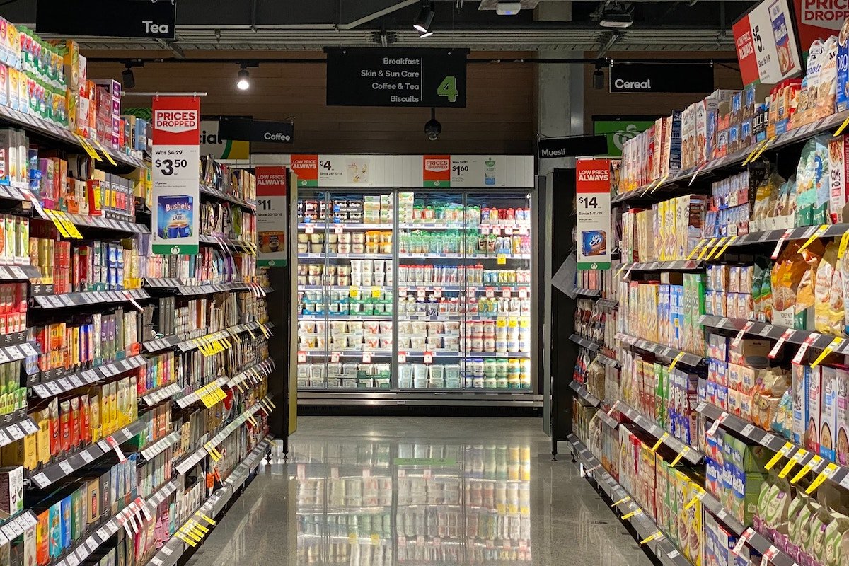 Looking down a grocery aisle with a concrete floor towards a row of refrigerators